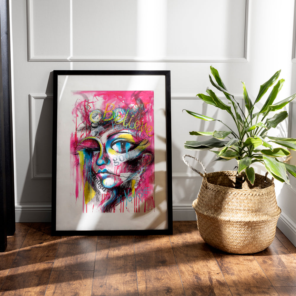 Believe in Yourself abstract portrait art print with graffiti-style text, bold magenta, yellow, blue, and black colors, featuring positive affirmations and collaged criticisms.
Shown in black frame in an interior