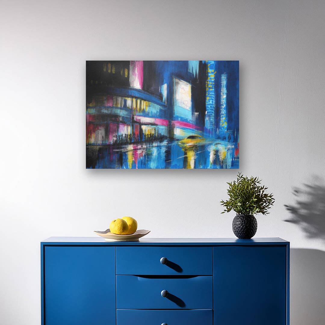 The City Reigns, urban nightscape painting with neon accents, displayed above a modern blue cupboard, adding a vibrant city vibe to the room."